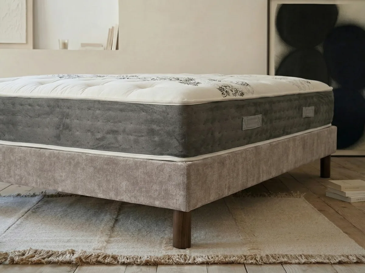Base para colchón: el matrimonio que decide cómo duermes 1 Colchón apoyado sobre un canapé rígido tapizado con patas de madera en un dormitorio